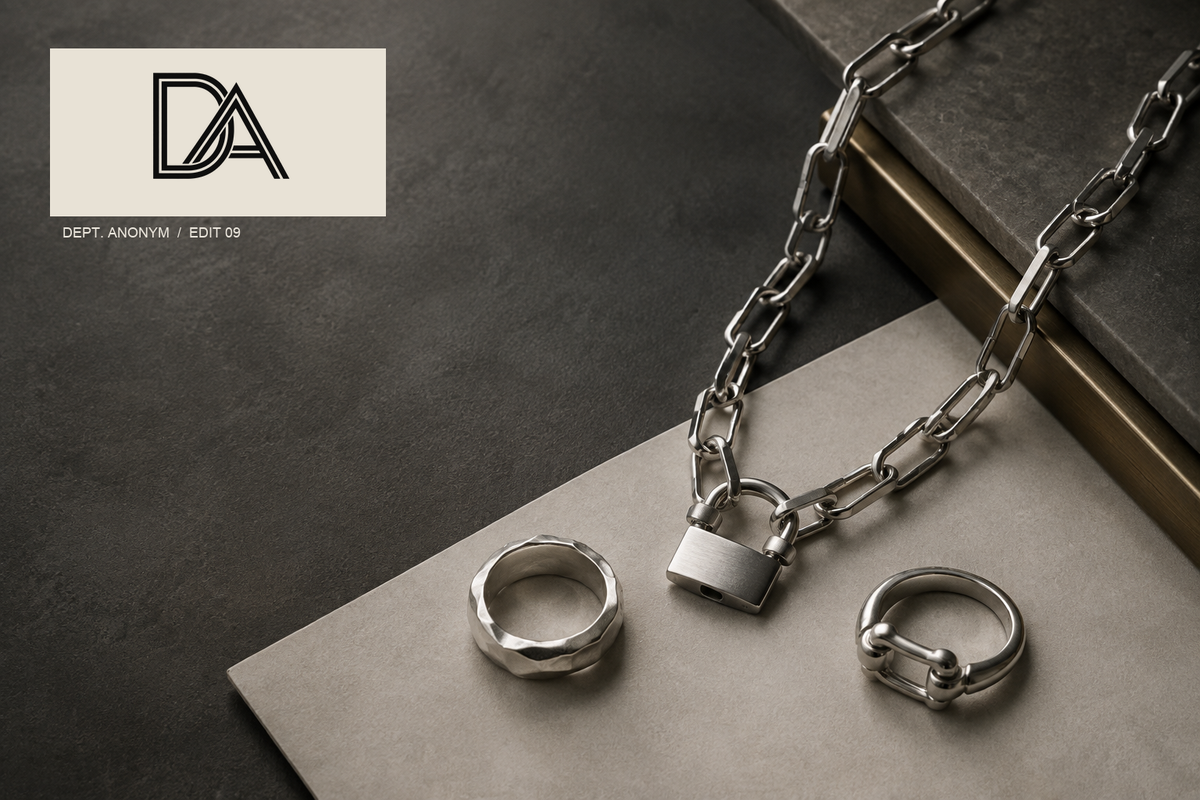 Original Dept. Anonym editorial still life of a chain necklace and two silver rings in graphite and bone tones, with the approved DA logo lockup; illustrative, not a product photograph.
